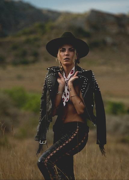 Woman in a stylish outfit with a hat and leather jacket standing in a natural setting