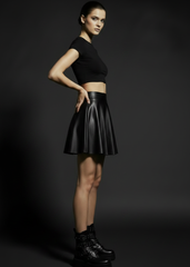 Black vegan leather mini skirt with flared A-line silhouette shown on model against dark gray studio background