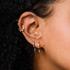 Close-up of an ear with gold hoop earrings and a small gold earring.