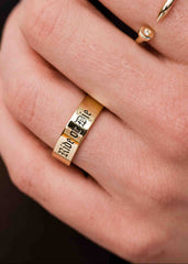 Gold ring with engraved text on a person's finger against a dark background