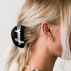 Close-up of a person wearing a black hair clip with white text and green earrings.