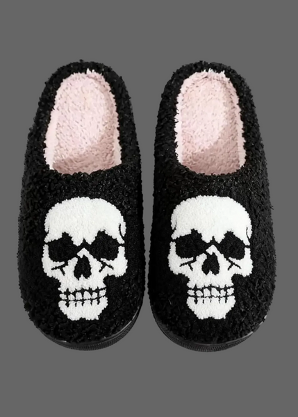 A pair of black fuzzy slip-on slippers with a white skull design on the front and a light pink plush lining inside, shown against a plain white background.