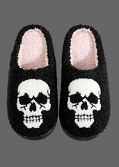 A pair of black fuzzy slip-on slippers with a white skull design on the front and a light pink plush lining inside, shown against a plain white background.