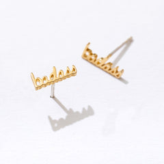 Gold 'badass' earrings on a white background