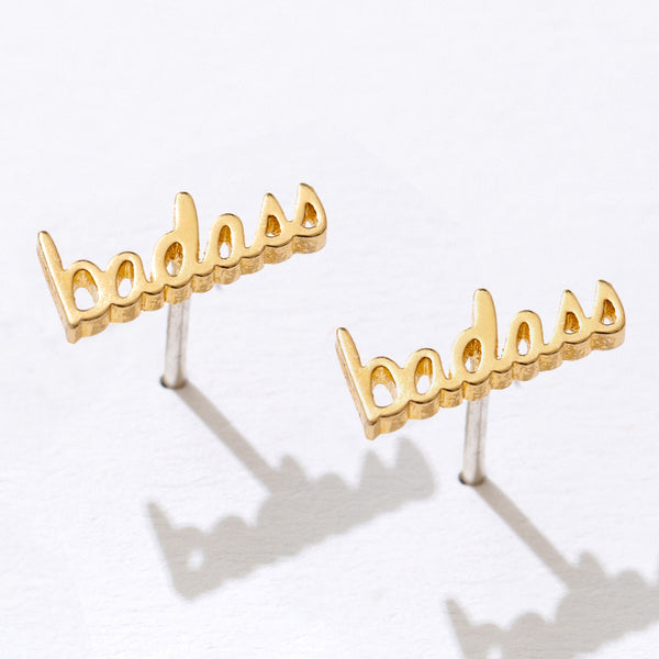 Gold 'badass' earrings on a white background