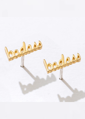 Gold 'badass' earrings on a stand with a white background