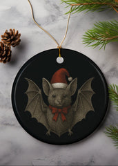Christmas-themed bat ornament with a Santa hat on a marble surface with pine branches and a gold ball.