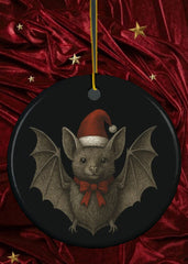 Bat wearing a Santa hat with red ribbon on a dark background, hanging from a string.