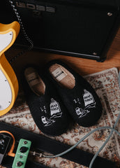 A pair of black slippers with 'Dead Tired' artwork, placed on a floor next to a guitar and amplifier.