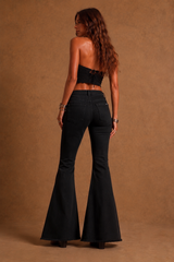 Woman wearing black flared jeans and a black top against a brown background