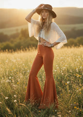  Model seated on a rock wearing rust bell bottom pants with wide flared hems and a cream cropped top.