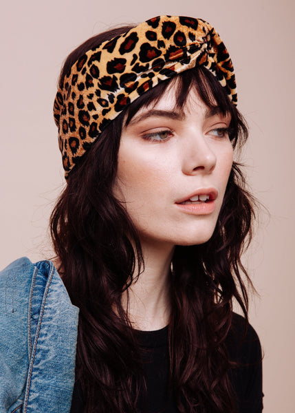 A person wearing a leopard print turban headband and a denim jacket.