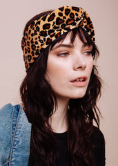 A person wearing a leopard print turban headband and a denim jacket.
