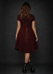 Alternative gothic burgundy skater dress with lace up back, metal button front and asymmetric hem styled with punk fishnet tights and combat boots