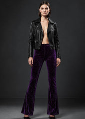 A model stands against a dark gray studio background wearing a black leather moto jacket and high-waisted, flared purple velvet pants.