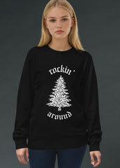 Woman wearing a black alternative Christmas sweater with a white Rocking around the Christmas tree graphic design on a dark background