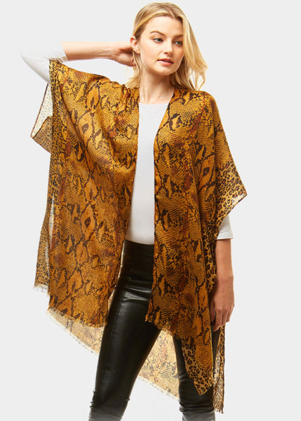 Woman wearing a patterned orange and black shawl over a white top and black pants on a white background